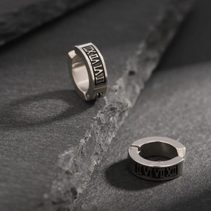 Macro detail of polished stainless steel ear cuff with engraved Roman numerals on rock background