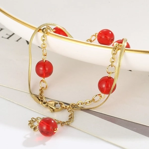 Detail view of a double-layer gold snake chain bracelet with elegant red beads on a plate