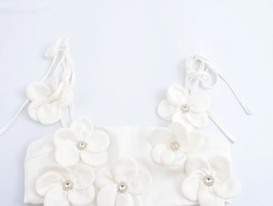 Close-up of white cropped camisole featuring 3D fabric flowers and crystal centers