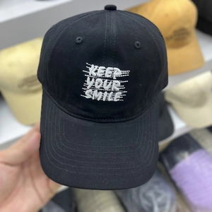 Detailed view of white Keep Your Smile embroidery on black cotton baseball cap