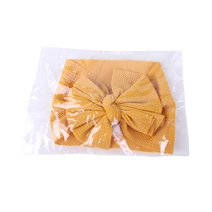 Macro detail of a yellow knitted baby headband with a large bow in plastic packaging