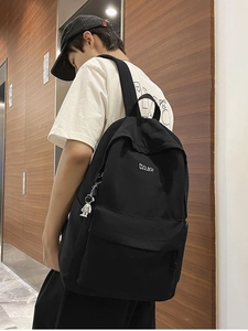 Minimalist black backpack with astronaut charm shown on a male model in a street setting