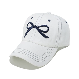Close-up of white baseball cap featuring navy blue embroidered bow and detailed stitching