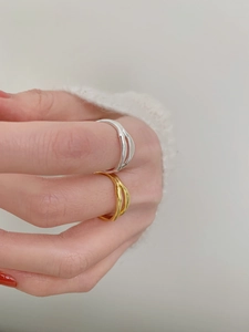 Detail shot of silver and gold irregular wavy rings worn with white knitwear
