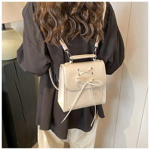 Detail of cream white leather backpack featuring a large bow and criss-cross ribbon design
