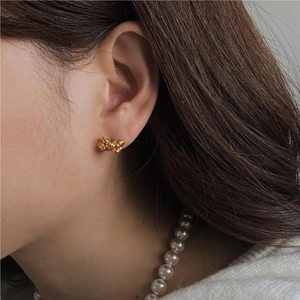 Close-up of elegant gold ribbon knot stud earring worn by model with pearl necklace