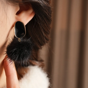 Detail macro of a golden oval earring with a plush black fur ball pom-pom on model