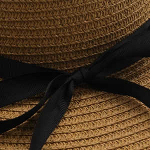 Detail of high-density straw weave texture and black grosgrain ribbon bow on a sun hat