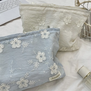 Detail of floral embroidery and branded tag on large cosmetic bags in blue and beige