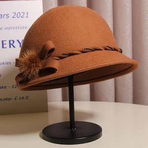 Elegant dark brown wool cloche hat with a bow and faux fur pompom on a display stand