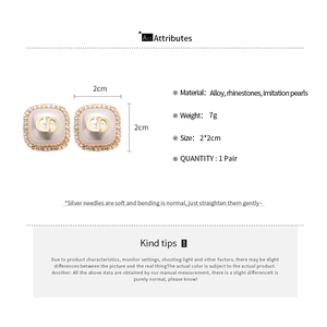 Macro view of square stud earrings with pearl base, gold CD logo and rhinestone halo