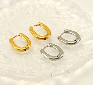 Close-up of gold and silver U-shaped chunky hoop earrings on a decorative glass tray