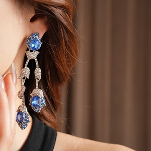 Close-up of model wearing vintage flower tassel earrings with blue gemstone in silver finish