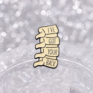 Skeleton spine enamel brooch pin with I'VE GOT YOUR BACK pun on bokeh background