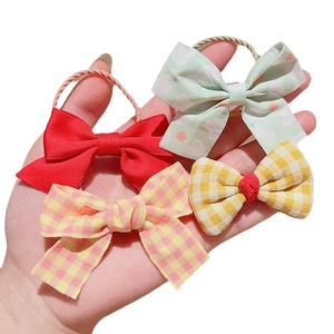 Child bow hair ties in red, green polka dot, and plaid patterns on palm