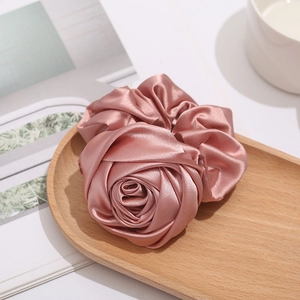 Elegant pink satin rose hair scrunchie with glossy finish on a wooden tray