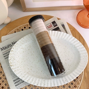 Detail of high-elastic seamless hair ties in a clear cylinder jar on a white ceramic plate