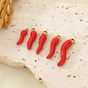 Detail of five red enamel chili pepper pendants in various sizes on a beige stone surface