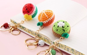 Handmade knitted fruit keychains featuring watermelon and orange on a notebook