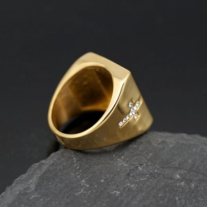 Men's gold-plated titanium cross ring set on a dark textured rock background