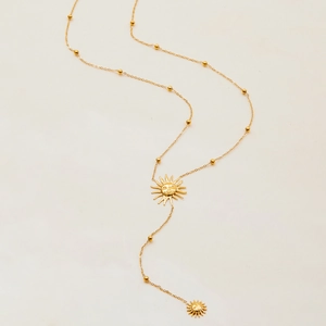 Collier en Y doré avec pendentifs soleil et petites perles sur fond beige épuré