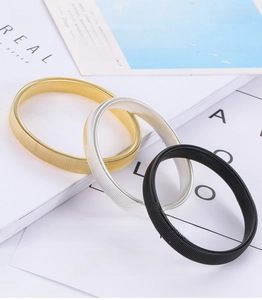 Detailed close-up of flexible metal spring armbands in gold, silver, and black finishes