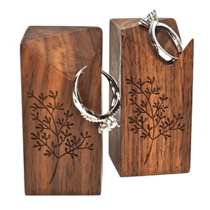 Pair of walnut cone ring holders with leaf engraving and silver rings on white background