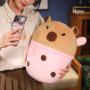 Plush brown capybara toy inside a pink bubble tea cup held by a young woman in home setting
