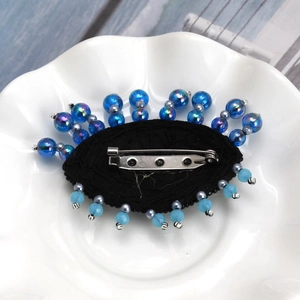 Detail of blue beaded evil eye brooch with back metal pin on a white ceramic dish