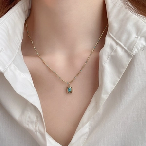 Detail of bohemian gold chain necklace featuring a turquoise rectangular pendant on a model