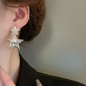 Detail of gold star drop earrings with brushed metal texture worn by a model