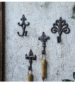 Detail of four vintage cast iron wall hooks with ornate rustic designs on concrete