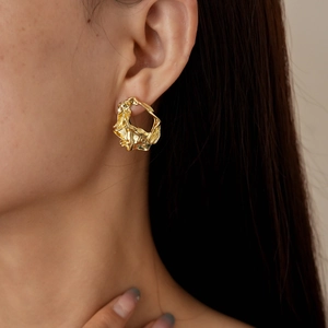 Close-up of golden irregular wrinkled metal earrings worn on ear with abstract geometric texture