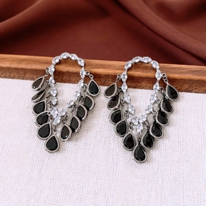 Close-up of silver earrings with sparkling crystals and black teardrop tassel pendants