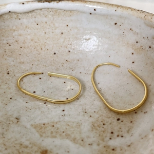 Macro detail of minimalist gold U-shaped oval hoop earrings on a ceramic dish