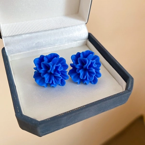 Close-up of blue resin flower stud earrings placed inside a dark blue jewelry gift box