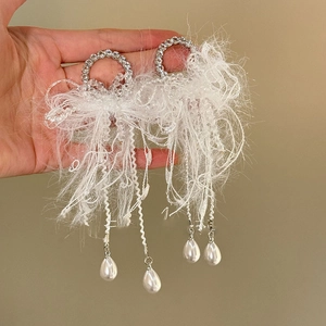 Detail of silver drop earrings featuring white feather tassels and round rhinestones