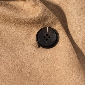 Macro shot of faux suede fabric texture and black four-hole button on the camel jacket