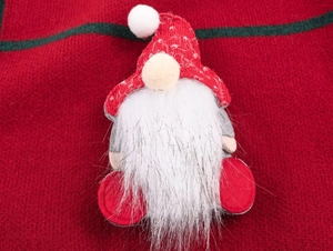 Macro detail of Christmas gnome plush featuring red knitted hat and long white faux fur beard