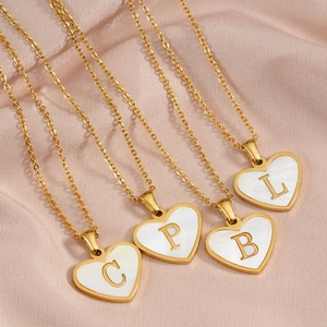Gold heart-shaped mother of pearl letter pendant necklaces on pink satin background