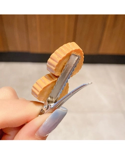 Detail view of the metal crocodile clip mechanism and wavy orange food-shaped hairpins