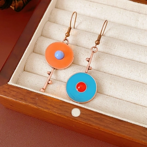 Macro detail of vintage enamel drop earrings with mismatched orange and blue round studs
