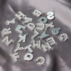 Detailed close-up of silver alphabet pendants with rhinestones on grey silk