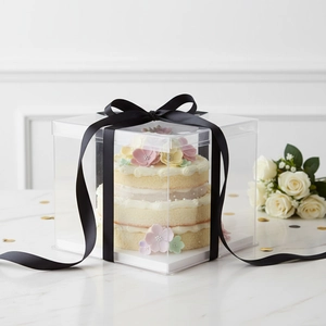 Elegant transparent cake box with black decorative ribbon on marble surface with white roses