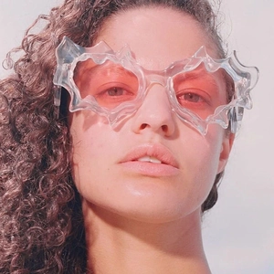 Detail view of avant-garde flame-shaped transparent sunglasses with pink lenses