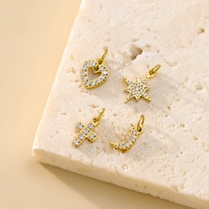 Close-up of four gold diamond-studded heart, star, cross, and moon pendants on a stone