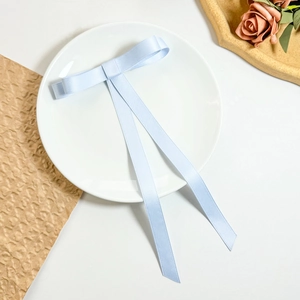 Close-up of a light blue satin ribbon bow hair clip with long streamers on a white plate