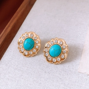 Dettaglio di orecchini vintage dorati con pietre turchesi e bordo di strass lucidi