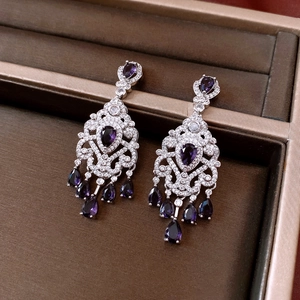 Macro shot of silver tassel earrings with purple drop stones on a dark velvet surface