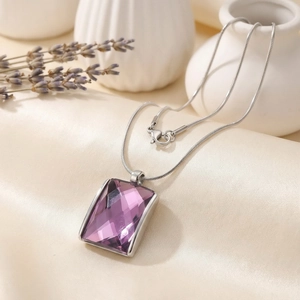 Detail of purple square glass pendant with silver snake chain on soft silk fabric